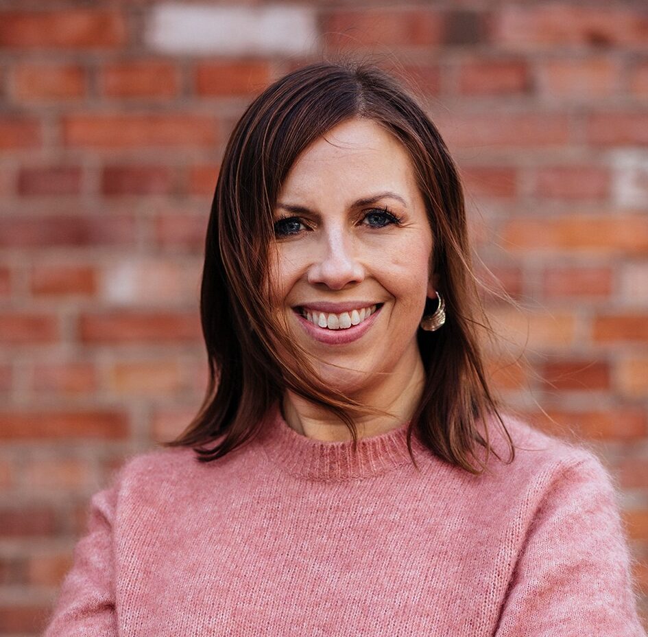 Maria står i en stickad tröja och ler in i kameran.