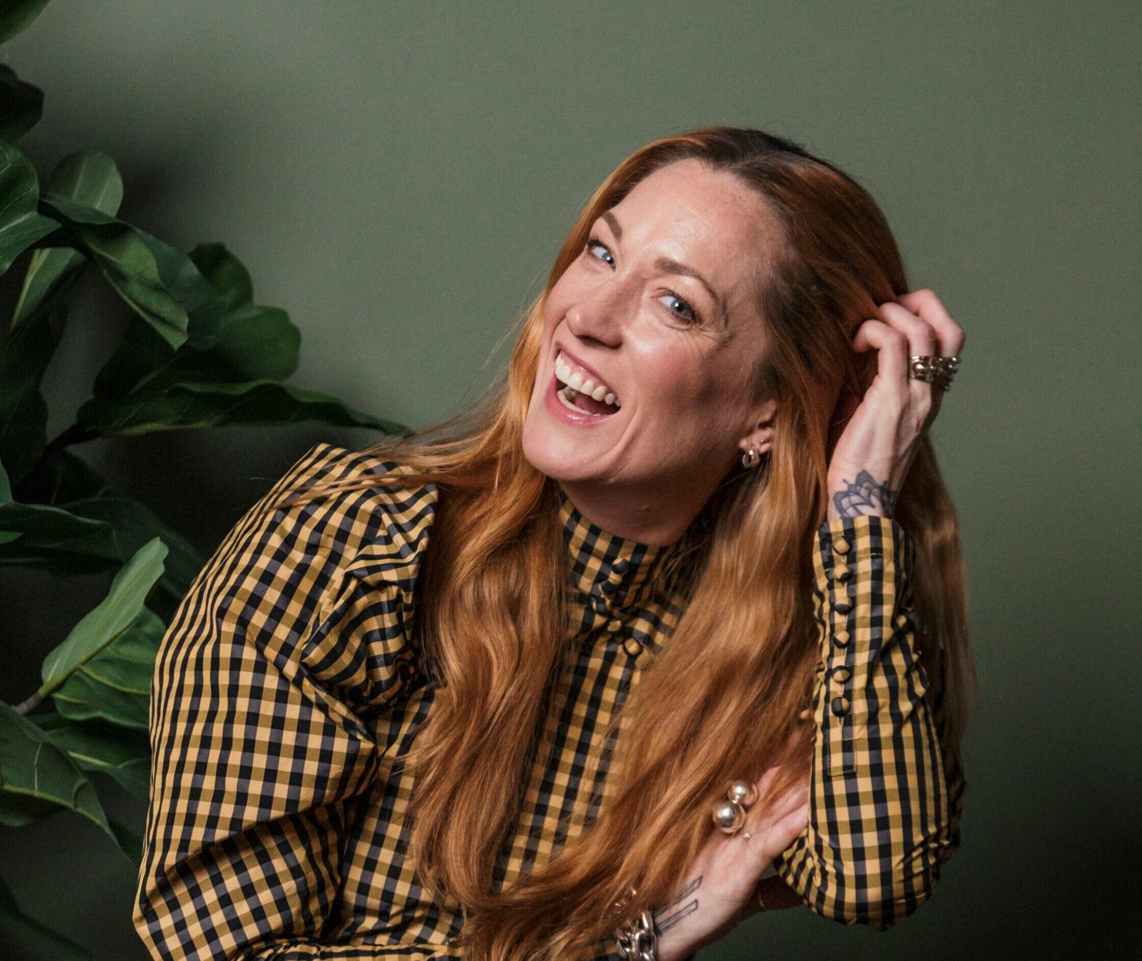 Lena Nyholm Lena sitter framför en grön vägg och skrattar in i kameran.